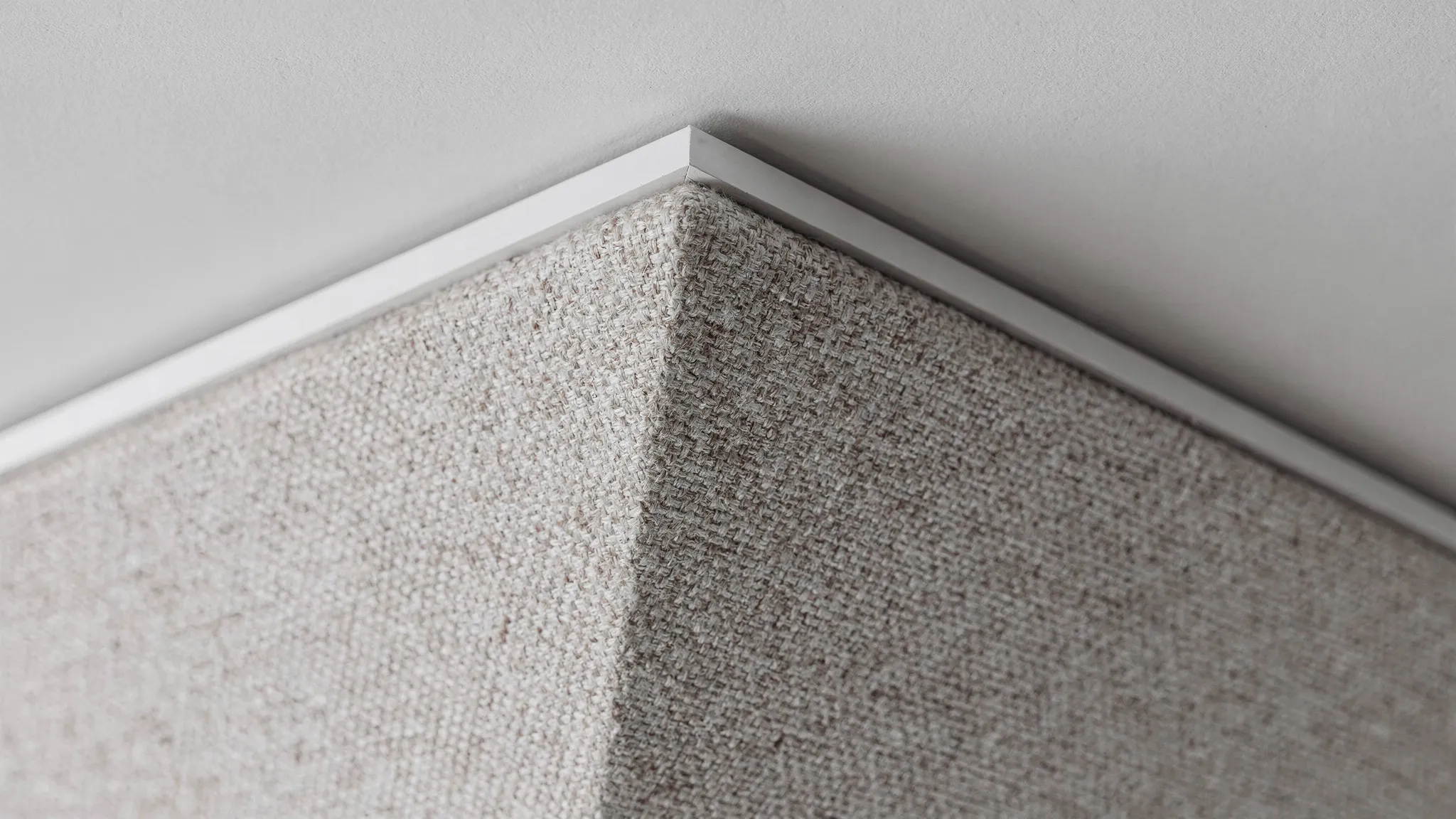 Close-up van een luxe akoestisch plafondpaneel met strakke textielafwerking, scherpe rand (facet) en nette aansluiting op een minimalistische plafondlijn.